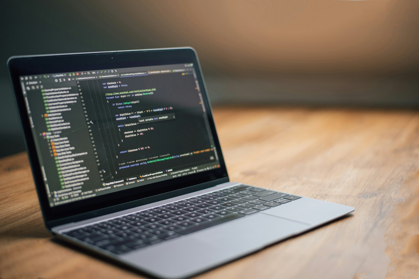 Laptop perak menampilkan kode pemrograman di atas meja kayu.